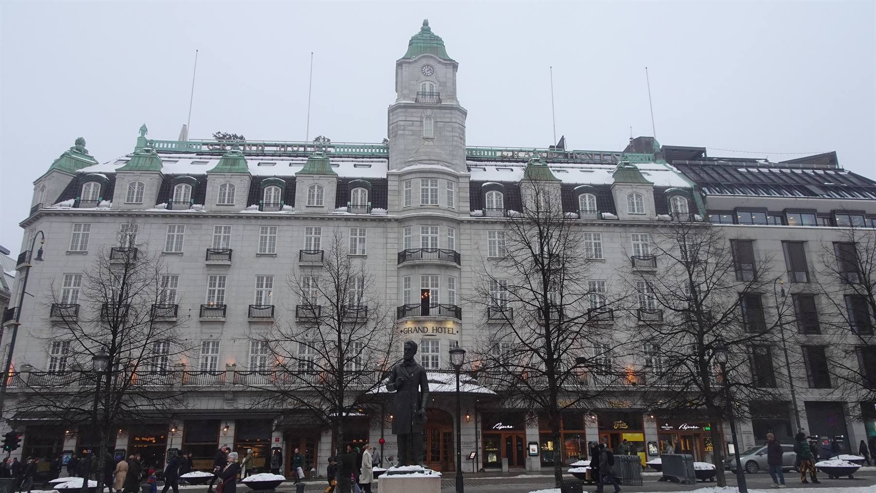 Statua davanti al Grand Hotel innevato a Oslo sotto cielo grigio