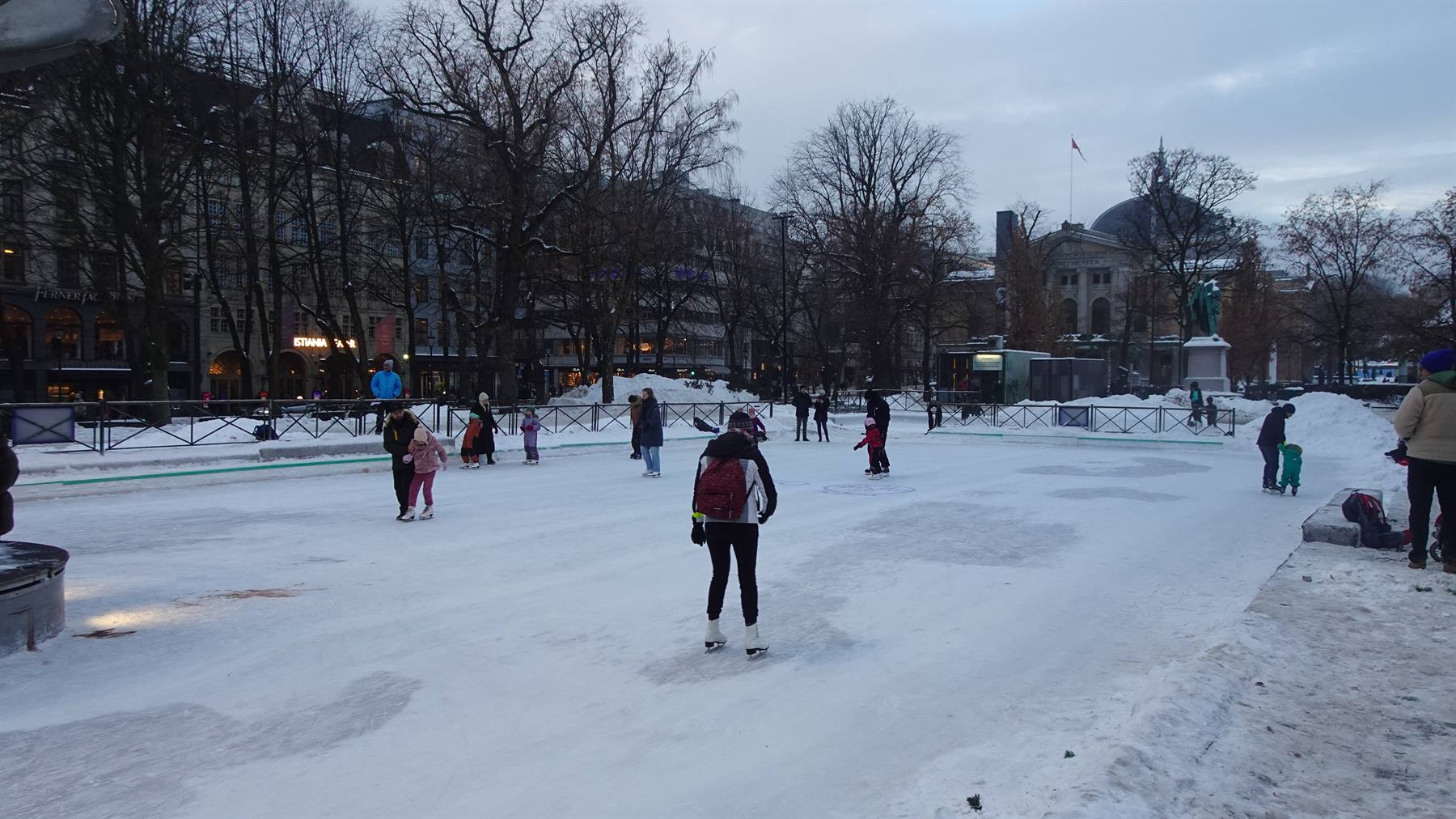 Pattinatori su pista di ghiaccio innevata in un parco cittadino, cielo grigio