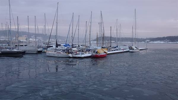Sailboats moored in a frozen harbor, snow-covered decks, grey winter light