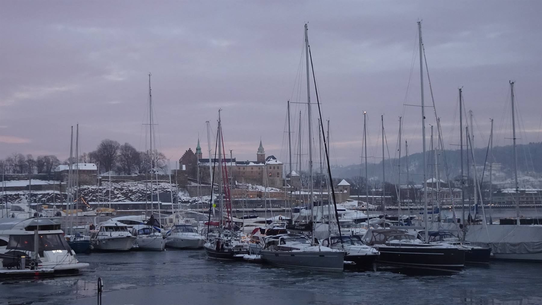 Barche a vela ormeggiate nel porto ghiacciato, fortezza innevata sullo sfondo, Oslo