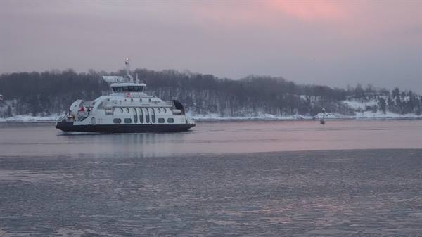 White ferry crossing icy waters, snowy shoreline behind under pink sky