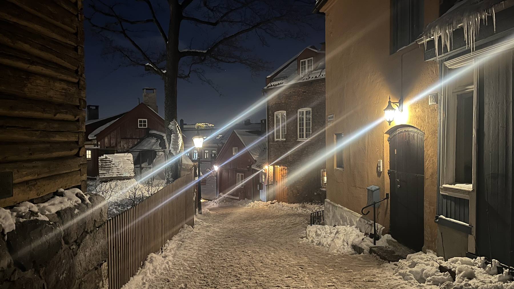 Vicolo innevato di Skansen a Stoccolma, case in legno e lampioni nella notte