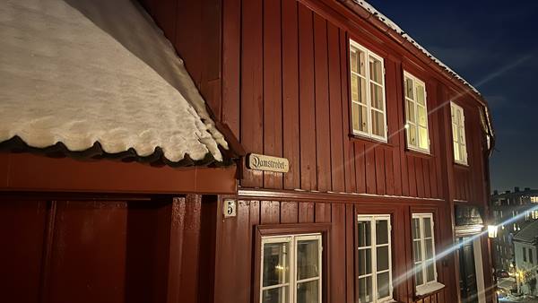 Red wooden house with snowy roof, Domkirkevegen sign, illuminated at night