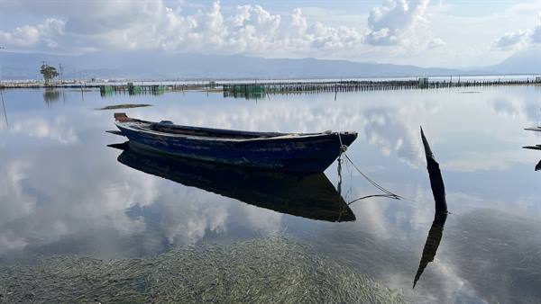 The boat sways silently, the sky mirrored in the calm water.