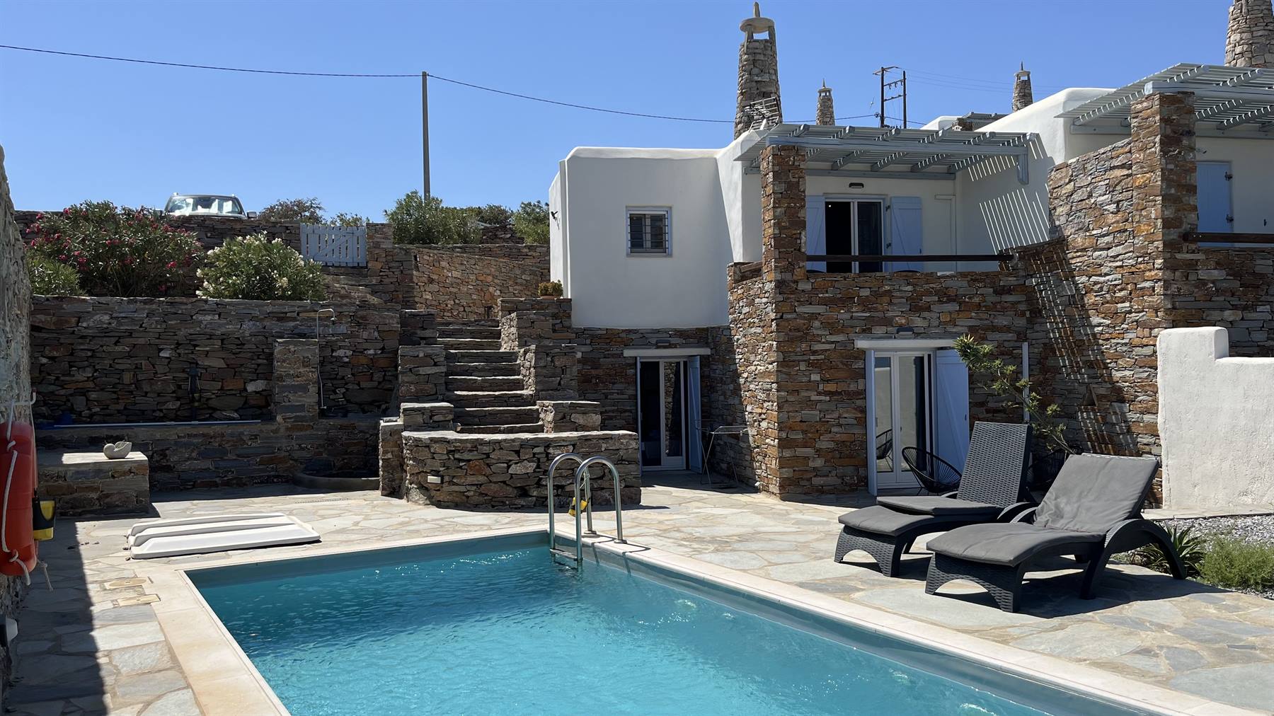 Piscina azzurra e sdraio davanti a case di pietra e calce, Cicladi