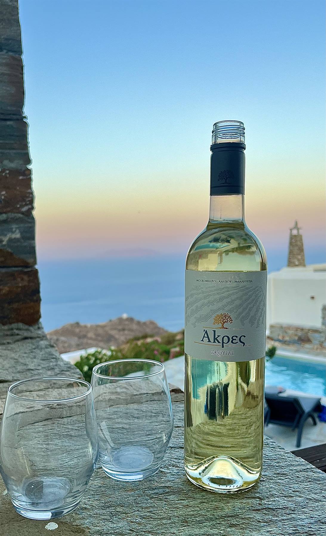 Bottiglia di vino bianco Akres con due bicchieri su muretto di pietra al mare