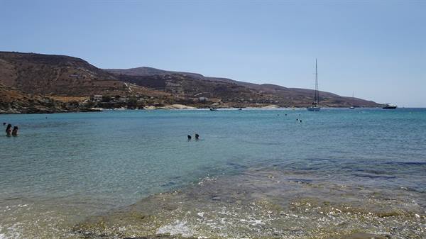Swimmers in turquoise water, dry hills behind, sailboats anchored offshore