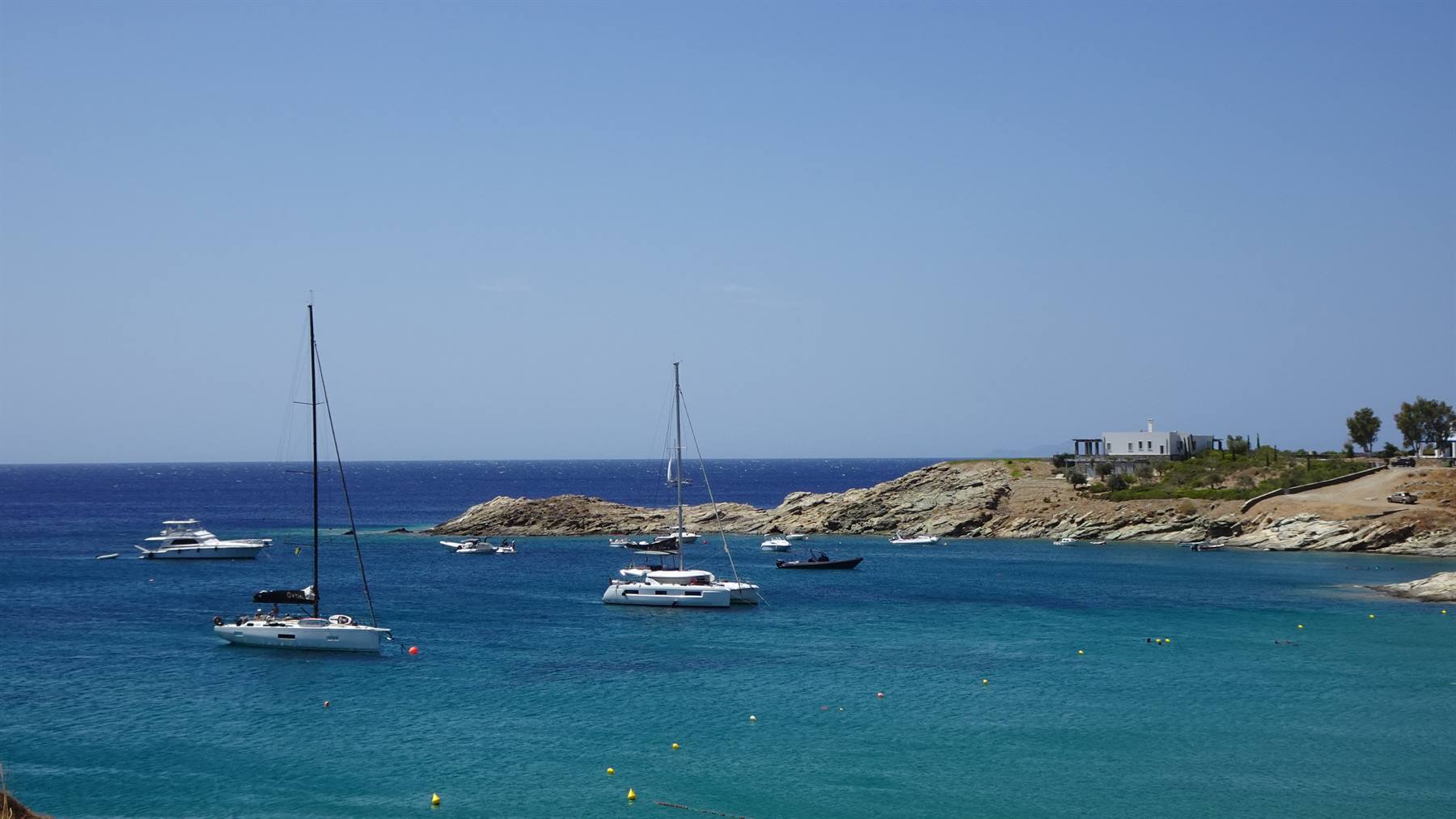 Vele e yacht ancorati in baia turchese, scogliere e case bianche sotto cielo azzurro