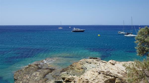 Sailboats and yacht anchored on turquoise sea in front of rocky cliffs