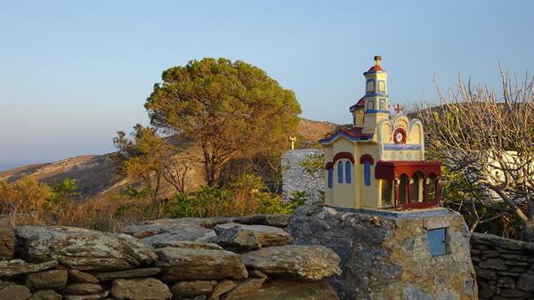 Small painted chapel on stone wall among hills and pine trees