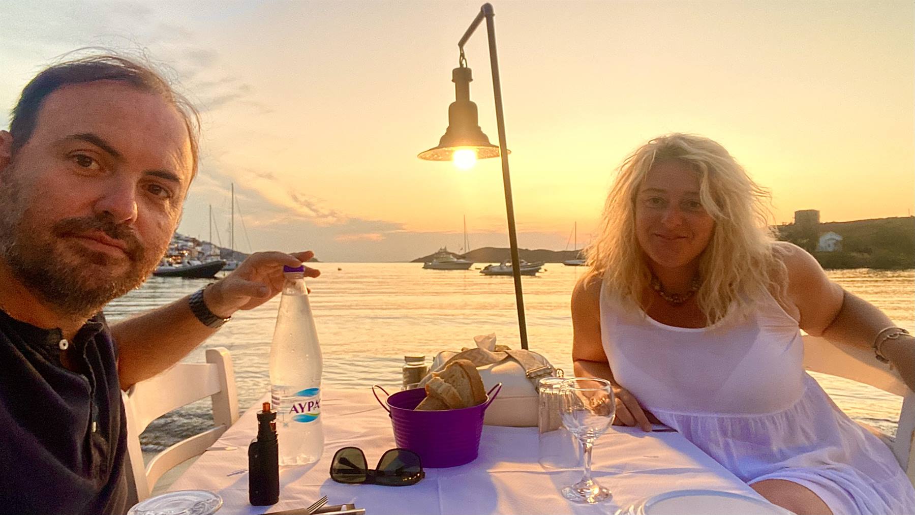 Coppia a tavola in taverna sul porto, bottiglia d'acqua e barca al tramonto