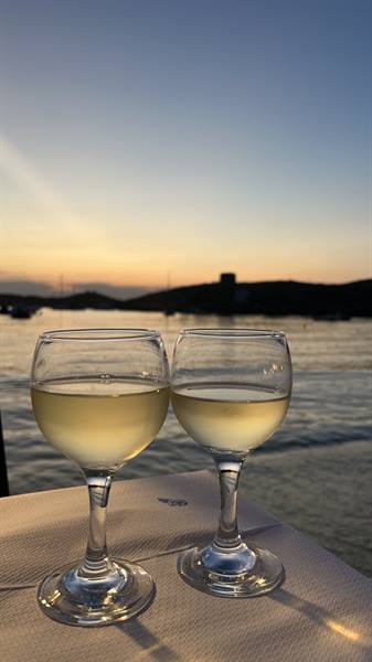 Two glasses of white wine on a table, sea and hills at dusk