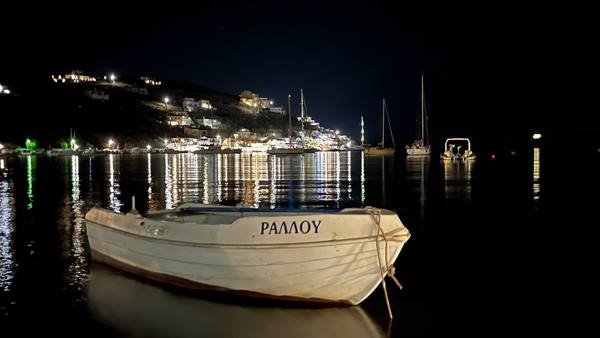 White wooden boat in foreground, lit harbor and moored sailboats at night