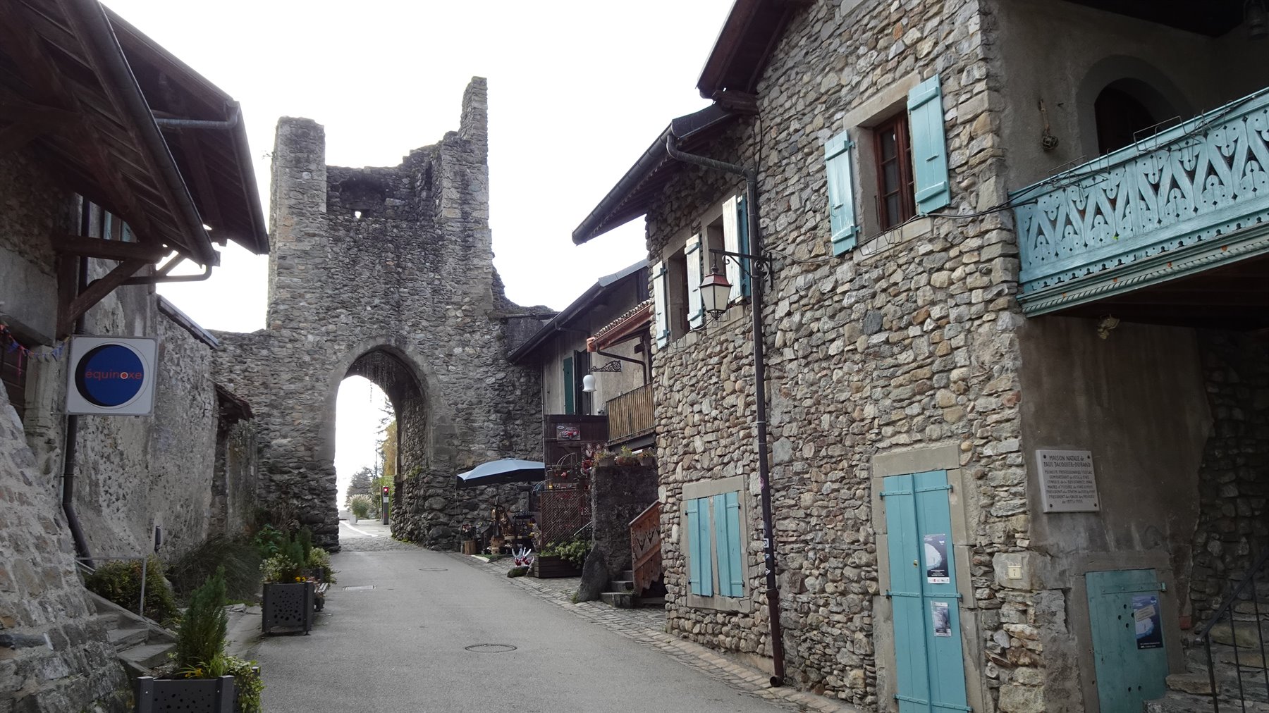 Porta antica in pietra e case con persiane turchesi nel borgo di Yvoire