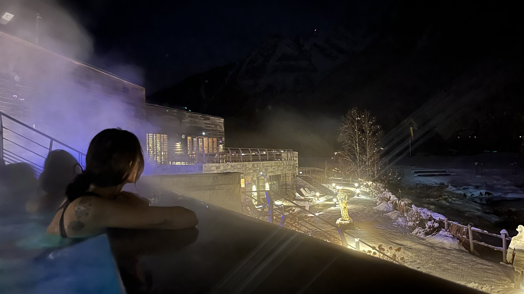 Donna in piscina termale all'aperto di notte, vapore e montagne innevate a Chamonix