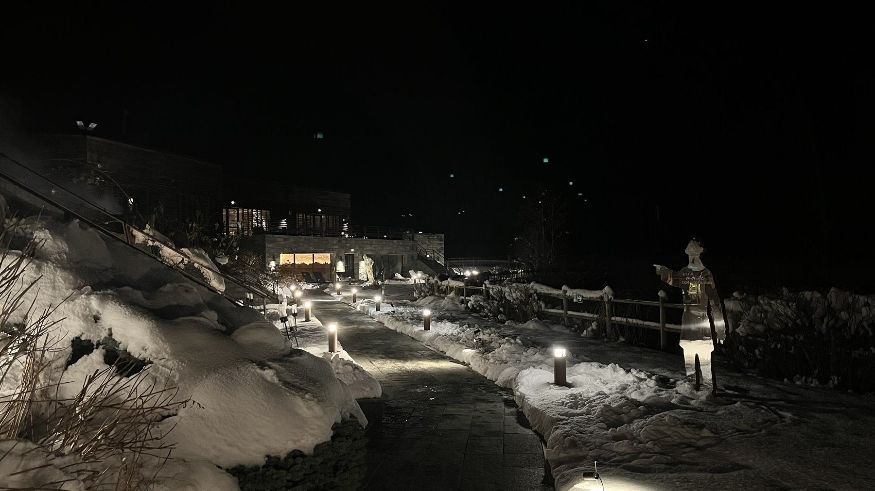 Sentiero innevato di notte con lampade luminose, statue e chalet illuminati a Chamonix