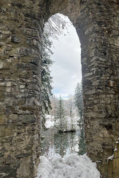 Snowy stone arch framing frosted trees and frozen pond, Col des Aravis