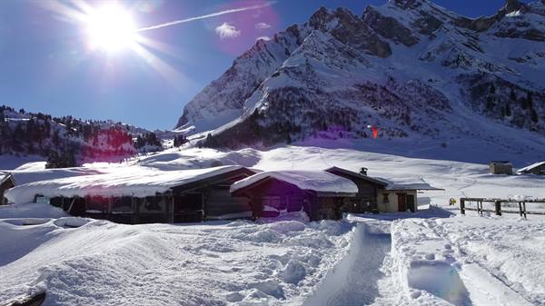 Snow-covered chalets under the sun at Col des Aravis, a paraglider over the peaks