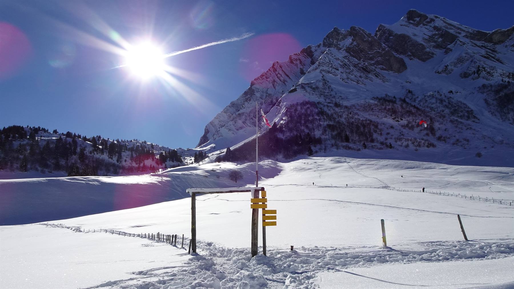 Sole su neve innevata e cartelli gialli sotto le vette, Col des Aravis