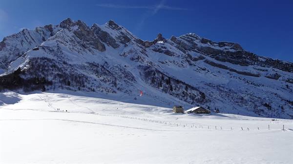 Wooden chalets on snow beneath the rocky peaks of Col des Aravis