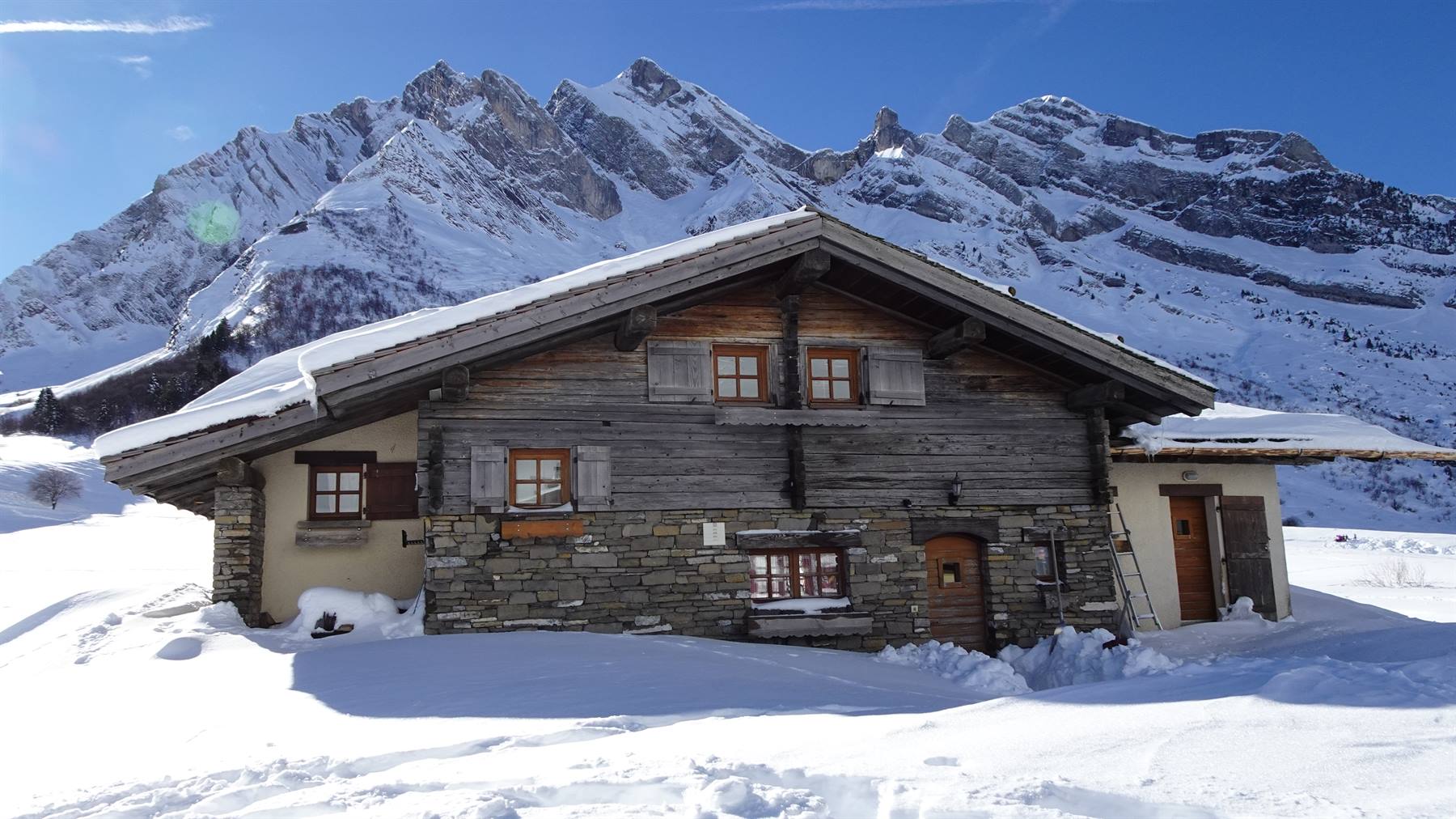Chalet in legno e pietra innevato sotto le montagne del Col des Aravis