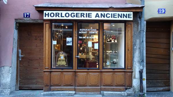 The wooden storefront of Horlogerie Ancienne with antique clocks on display