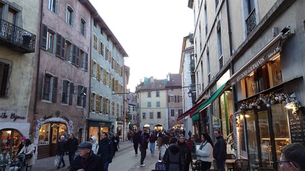 Crowded pedestrian street lined with colorful old buildings and shops, Annecy
