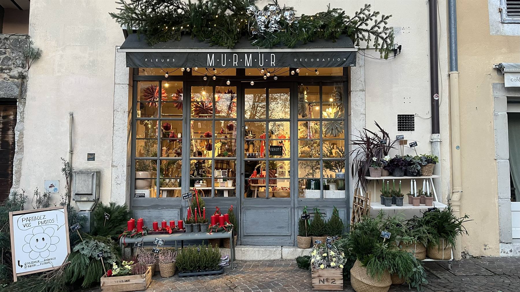 Bottega MurMur a Yvoire, vetrina in legno con piante, candele rosse e luci natalizie