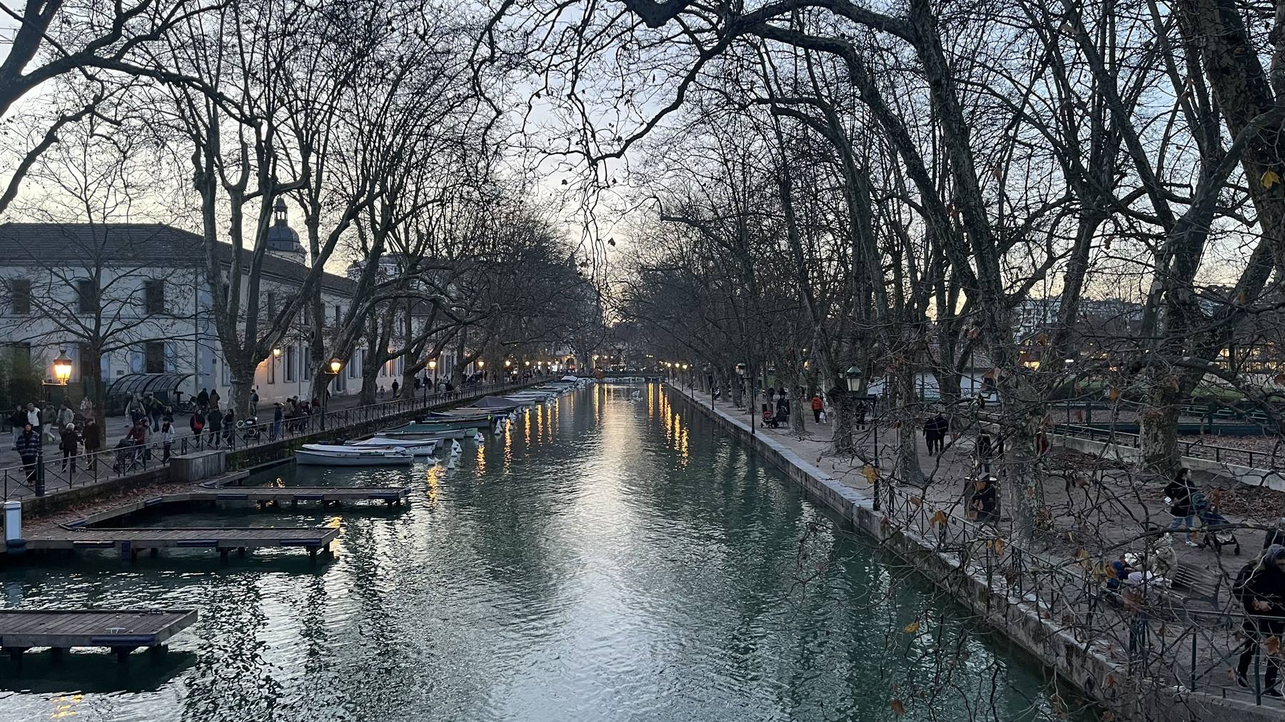 Canale con barche ormeggiate e alberi spogli, luci serali ad Annecy