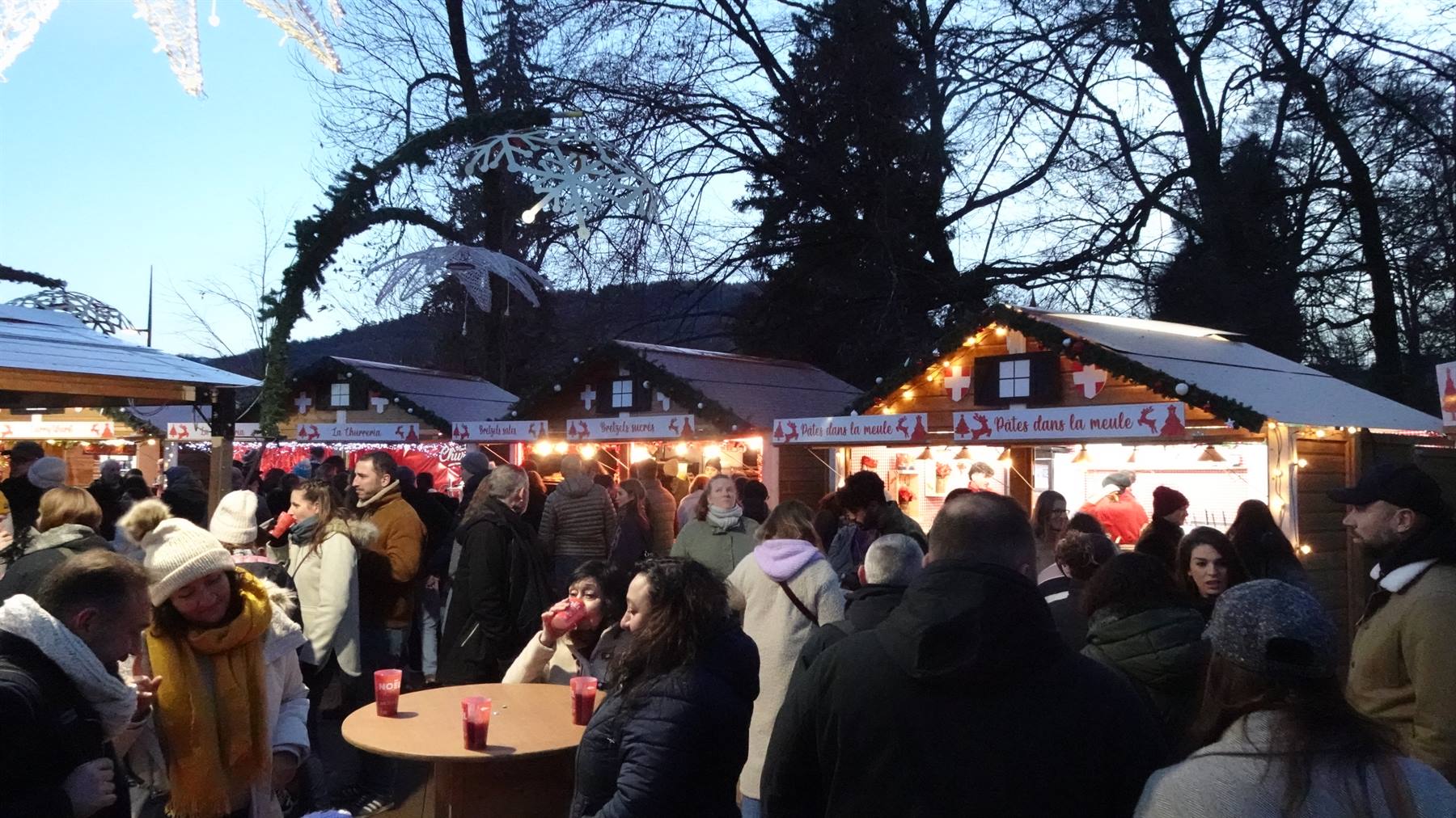 Mercatino di Natale a Annecy, visitatori con tazze di vin brulé tra chalet illuminati