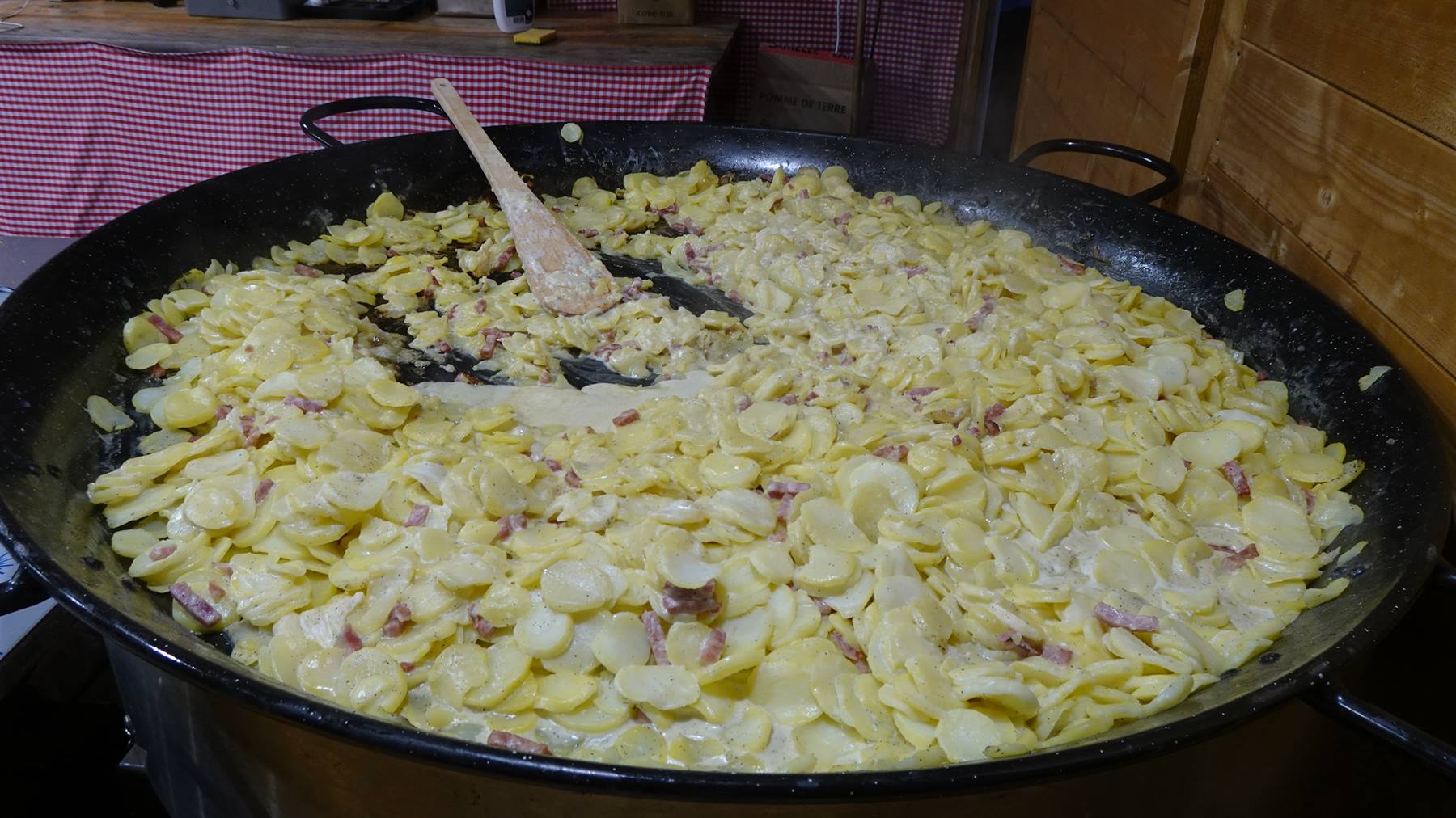 Padella gigante di tartiflette: patate, lardo e formaggio fuso mescolati con mestolo di legno