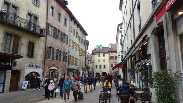 Pedestrians walking Annecy old town street among historic facades and cafes