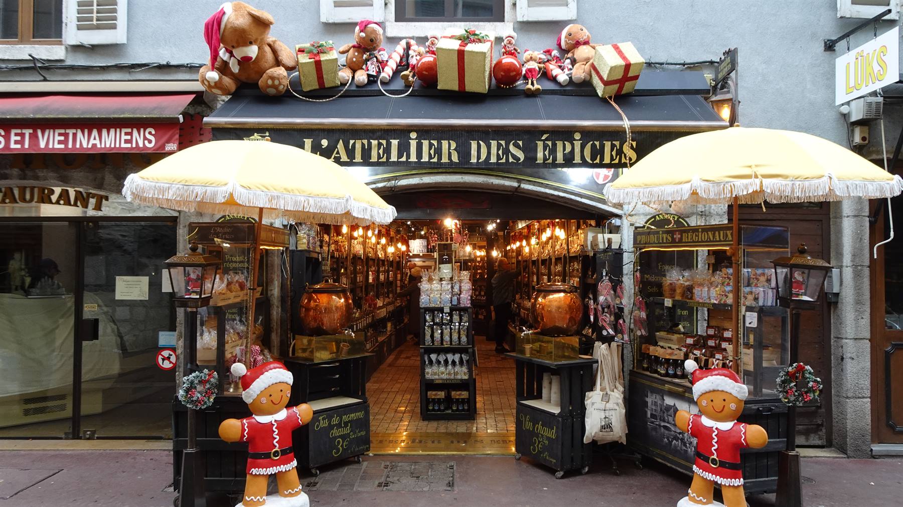 Ingresso di L'Atelier des Épices a Yvoire, con ombrelloni gialli e pupazzi di Natale