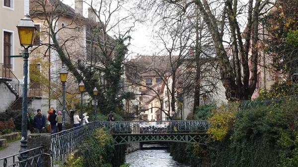 Tourists along the canal in Annecy, iron footbridge among bare trees