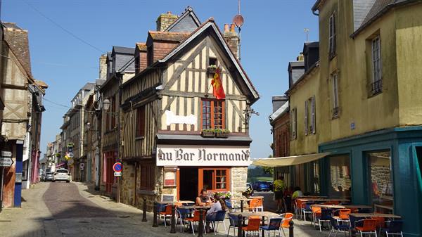 Half-timbered house with Au Bar Normand sign, outdoor café tables in sunny street