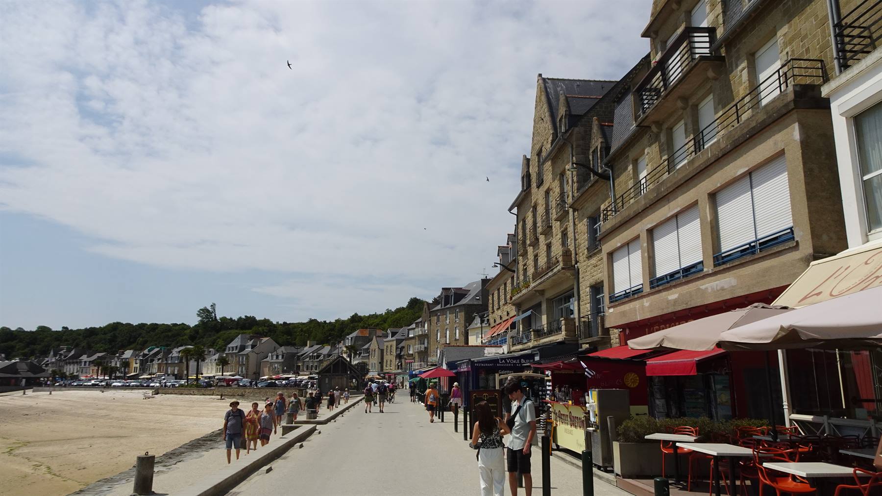 Lungomare di Cancale, case in pietra, ombrelloni rossi dei ristoranti, passeggiatori sulla banchina
