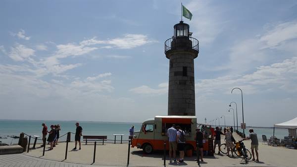 Crowd around a food truck beneath the stone lighthouse on Cancale pier