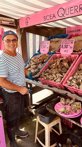 Smiling vendor with Cancale oysters in pink crates at market