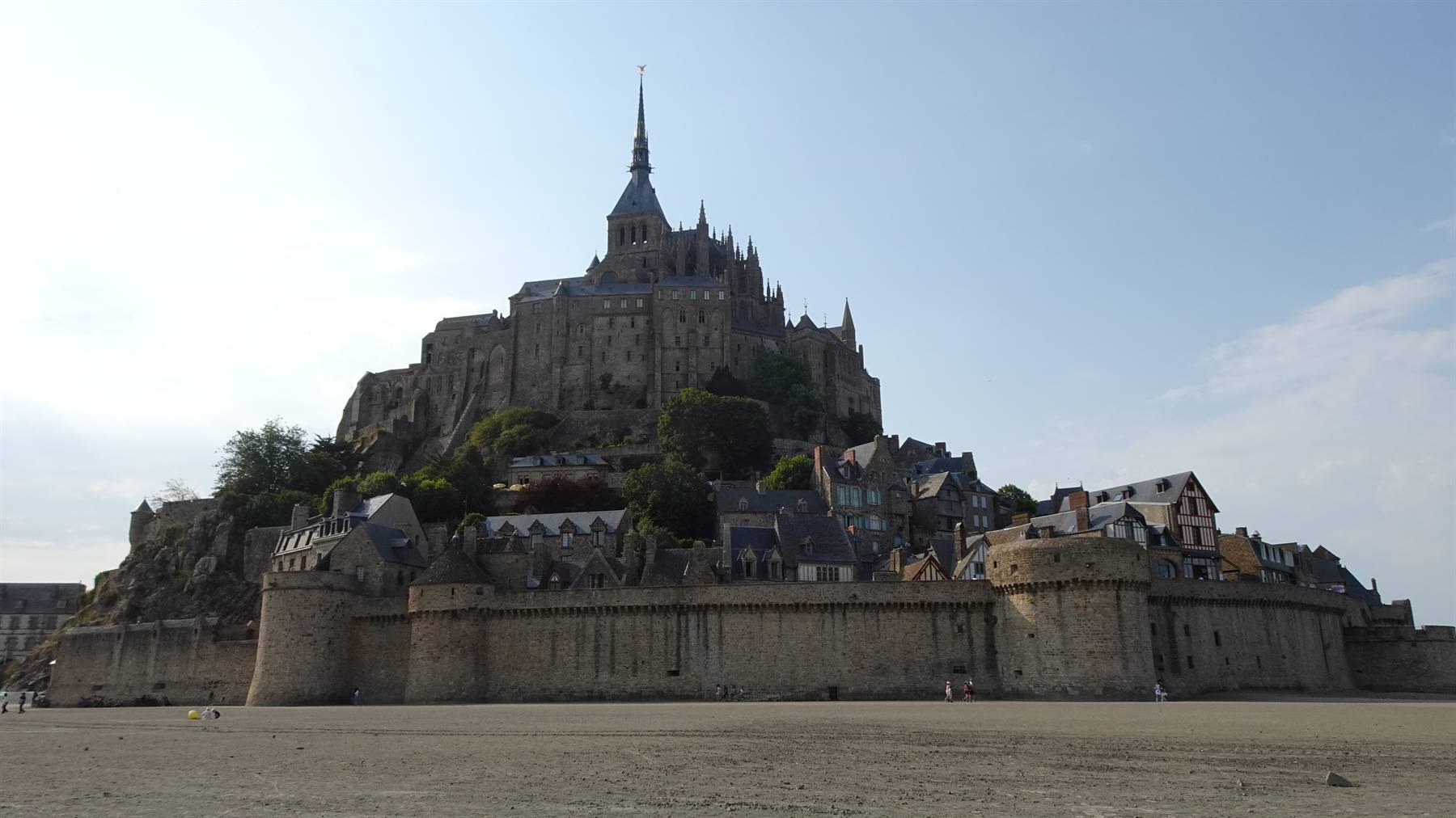 Mont Saint Michel: abbazia e mura in pietra sull'isola, sabbia e cielo chiaro