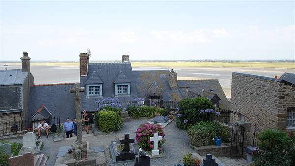 Cemetery with crosses and flowers above Mont Saint-Michel slate houses facing the bay