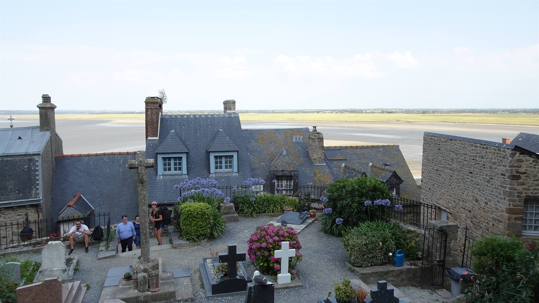 Cimitero con croci e fiori sopra le case di ardesia di Mont Saint-Michel sulla baia