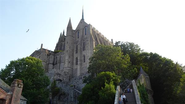 Mont Saint Michel abbey rising on rock, tourists climbing stone stairway