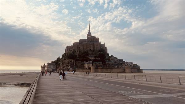 Visitors walk the causeway toward Mont Saint Michel abbey amid sands and clouds