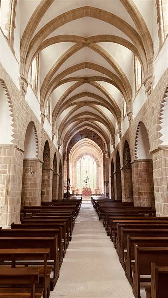 La Lucerne abbey church: stone vaults, wooden pews, light through stained glass