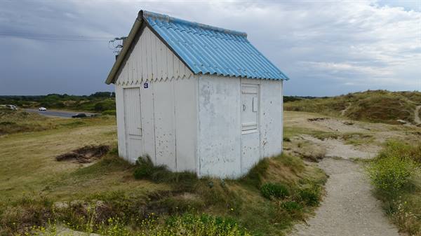 Small white wooden hut with blue corrugated roof on grassy dunes, Gouville sur Mer