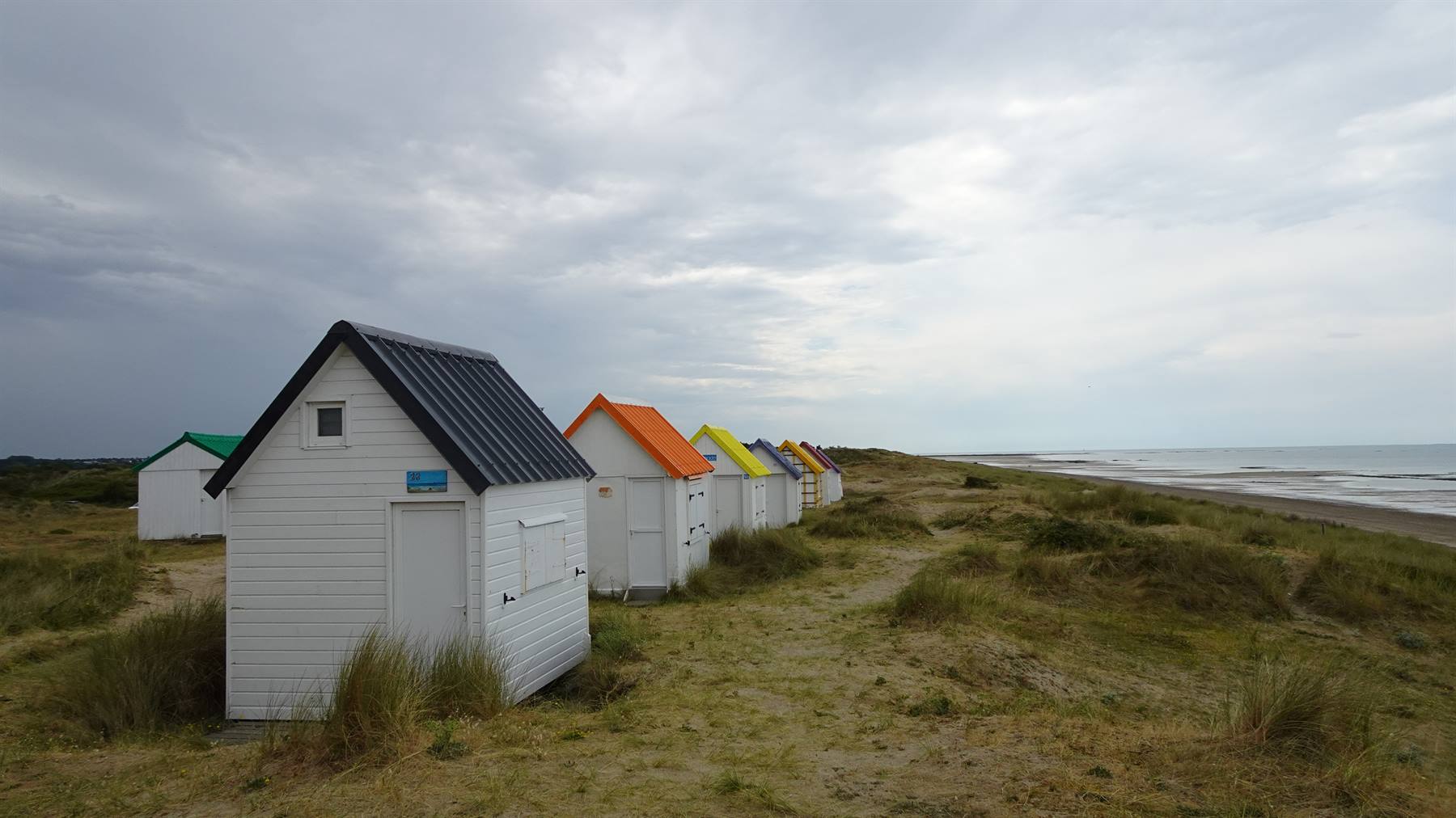 Cabanine in legno bianco dai tetti colorati tra le dune erbose di Gouville sur Mer