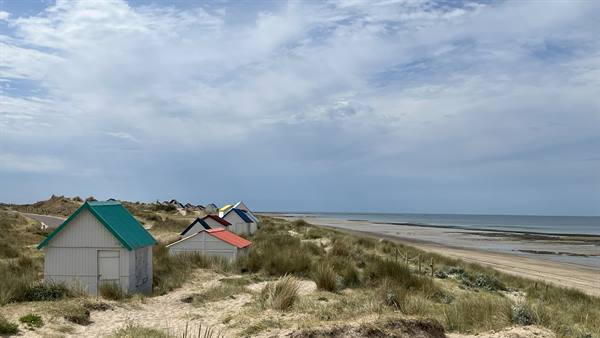 Colorful beach cabins on grassy dunes at Gouville sur Mer, low tide under clouds