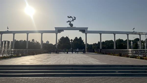 Turisti camminano sotto l'arco bianco con le gru, Tashkent, luce accecante