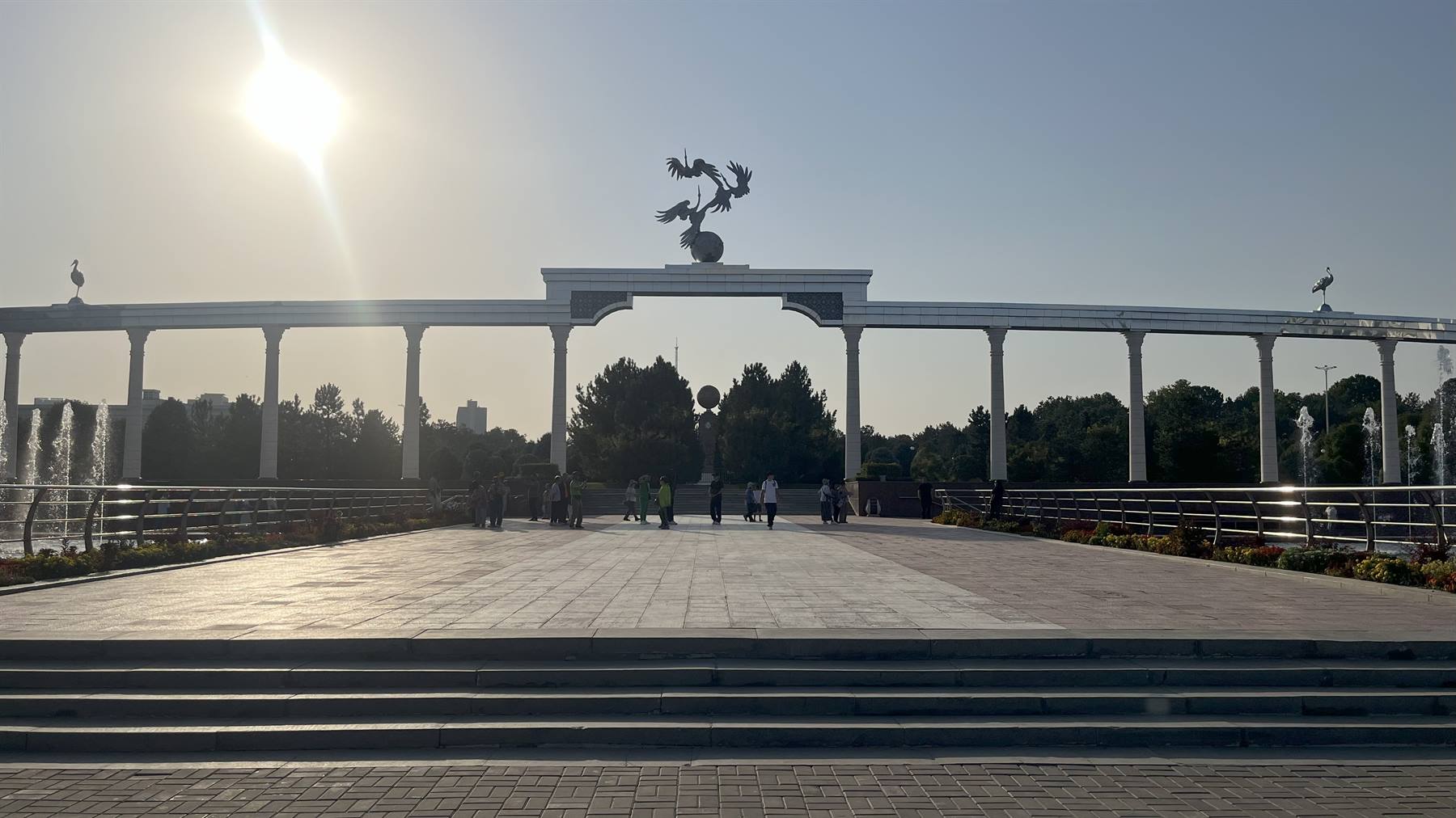 Turisti camminano sotto l'arco bianco con le gru, Tashkent, luce accecante