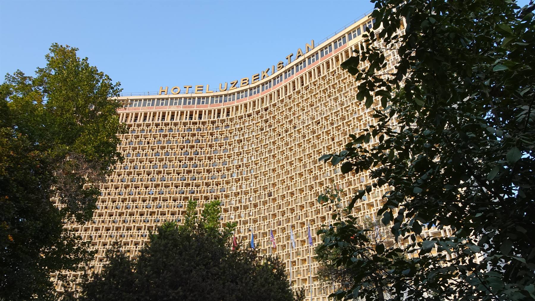 Facciata sovietica dell'Hotel Uzbekistan tra gli alberi verdi di Tashkent